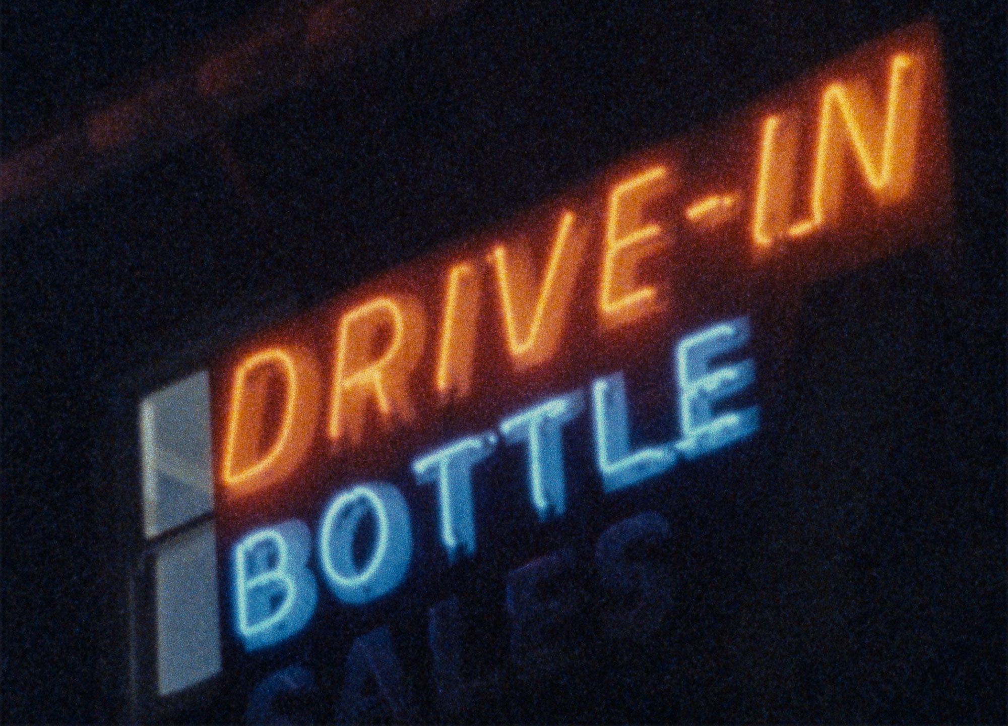 A neon sign, in red and blue, shot at night at the Strathfield Hotel which reads DRIVE-IN BOTTLE